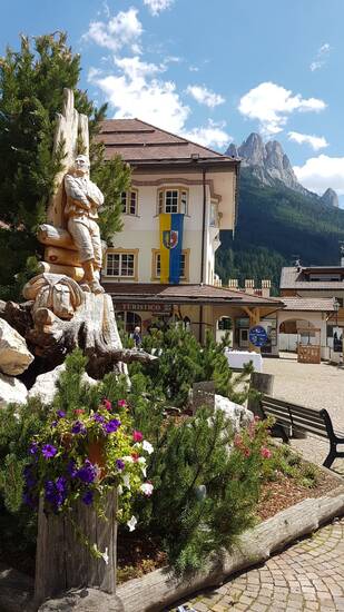 Im Vordergrund eine Statue im Blumenbeet, dahinter ein Gebäude.