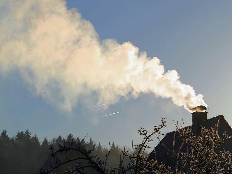 Haus mit rauchendem Kamin vor blauem Himmel.