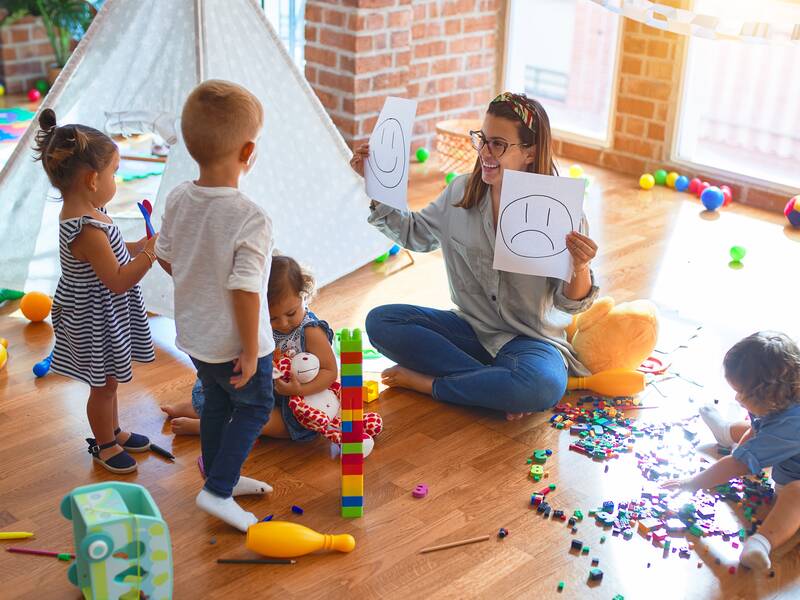 Spielende Kinder in einem Raum mit einer erwachsenen Person.