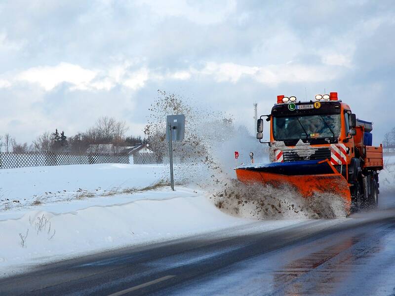 Schnee auf der Straße und ein Schneeräumfahrzeug beseitigt diesen.