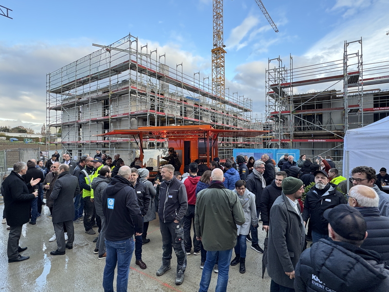 Menschen auf einer Baustelle, im hintergrund Häuser und ein Kran.