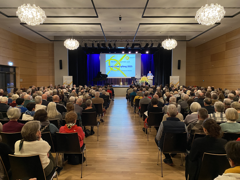 Stadthalle mit vielen Besuchern und einem Vortrag auf der Bühne.