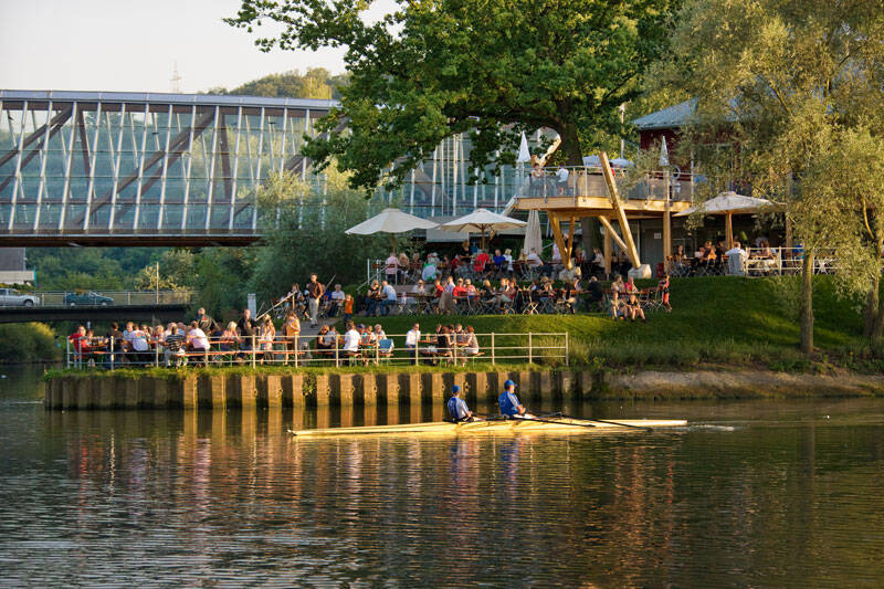 Ruderer auf dem Neckar am Hechtkopf an der Remsmündung im Hintergrund der Biergarten und die Remsbrücke