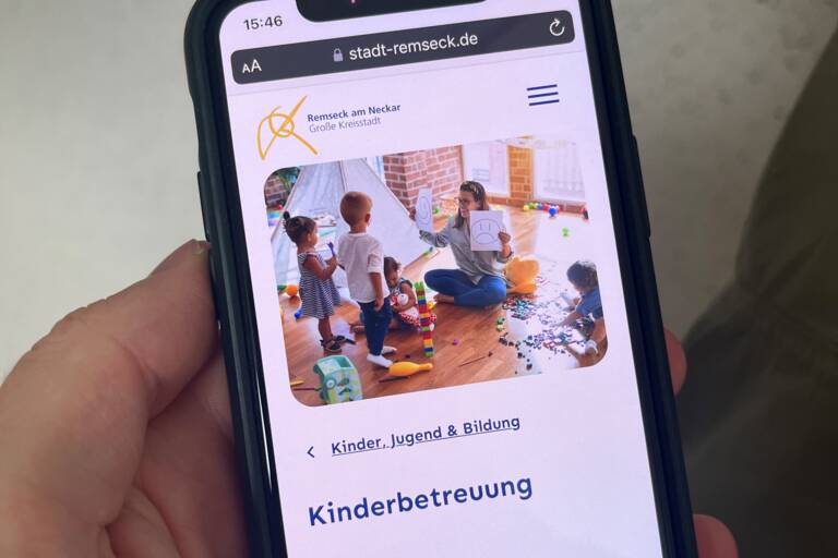 Ein Handy in einer Hand. Darauf ist die Seite "Kinderbetreuung" der städtischen Homepage abgebildet.