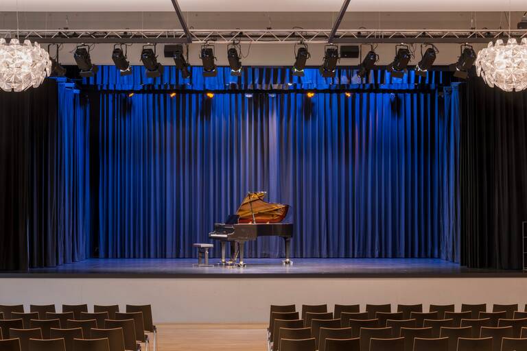 Bühne in der Stadthalle mit Flügel in der Mitte, im Vordergrund Reihenbestuhlung.