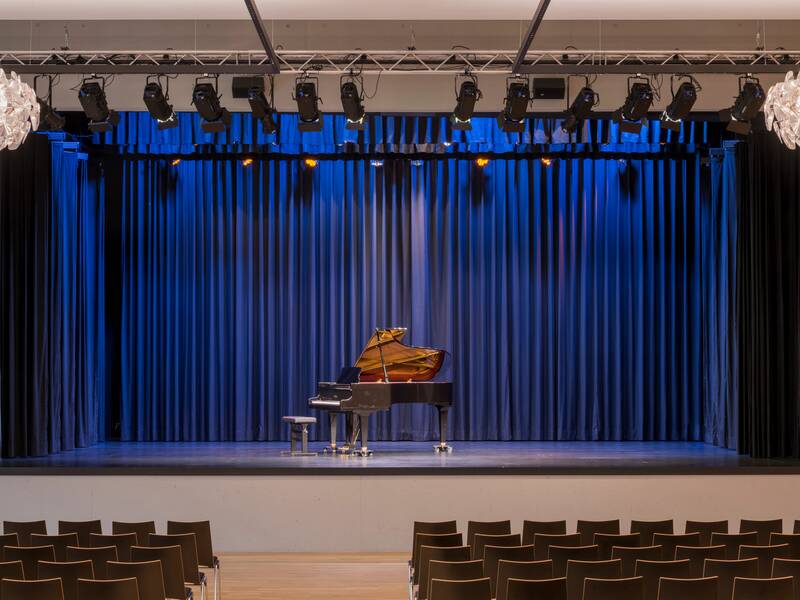 Bühne in der Stadthalle mit Flügel in der Mitte, im Vordergrund Reihenbestuhlung.