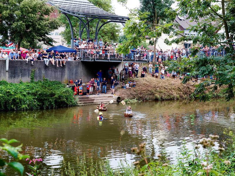 Fluss im Vordergrund mit Menschen die darin sind und weiter hinten Zuschauer.