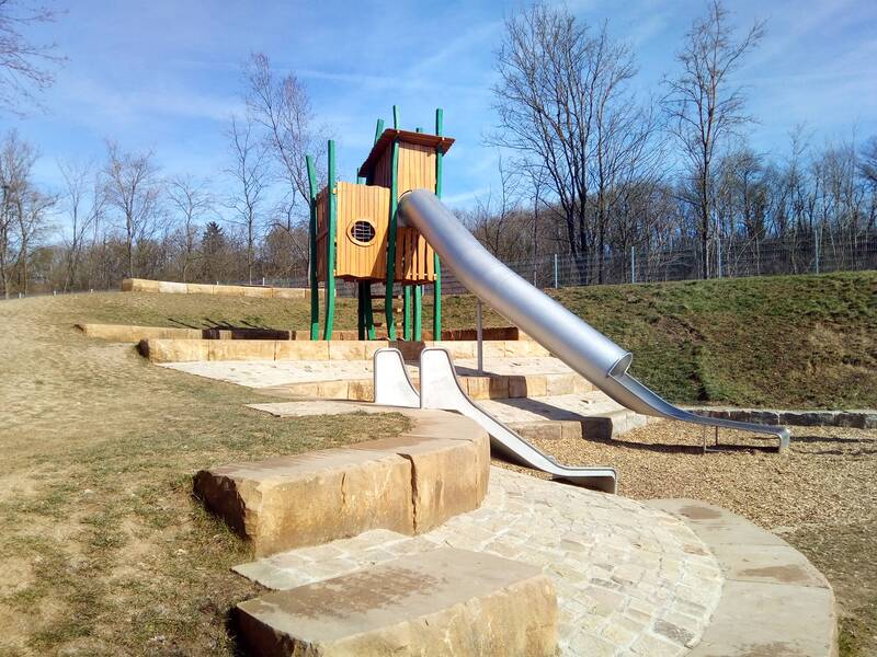 Rutsche auf einem Spielplatz, im Vordergrund ein Sandkasten.