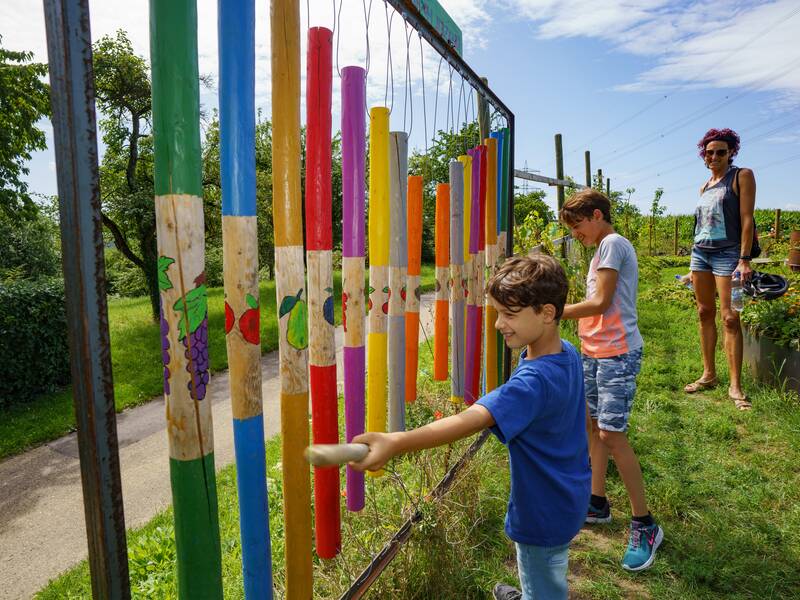 Zwei Kinder spielen an einem großen Glockenspiel aus bemahlten Holzstämmen.