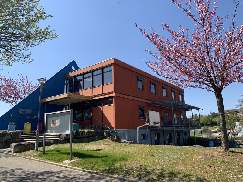 orangefarbenes Gebäude mit einem blauen, dekorativen Dreieck. Im Hitergrund ist blauer Himmel