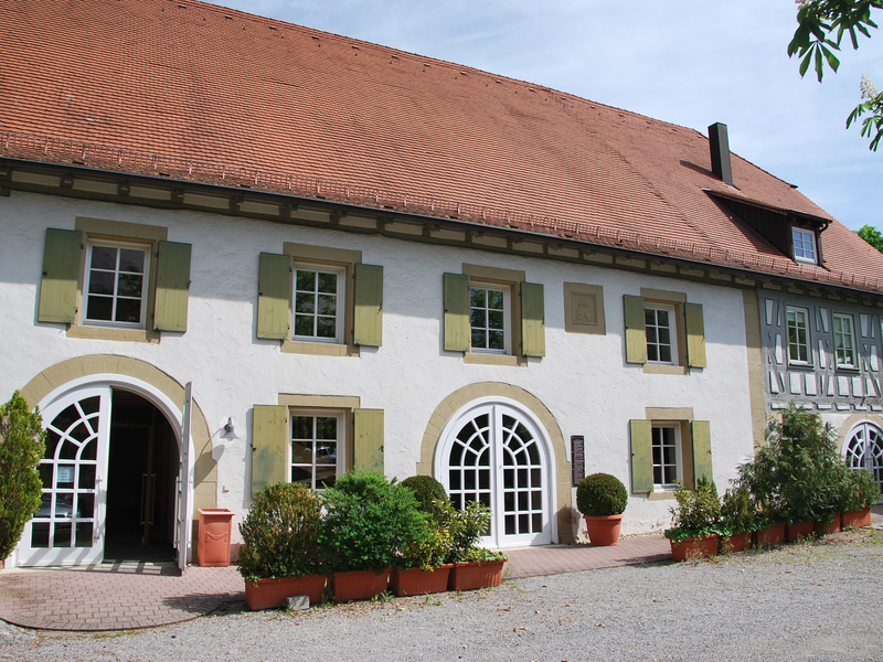 Alte Gemeindehalle Hochberg von außen bei sonnigem Wetter und blauem Himmel.