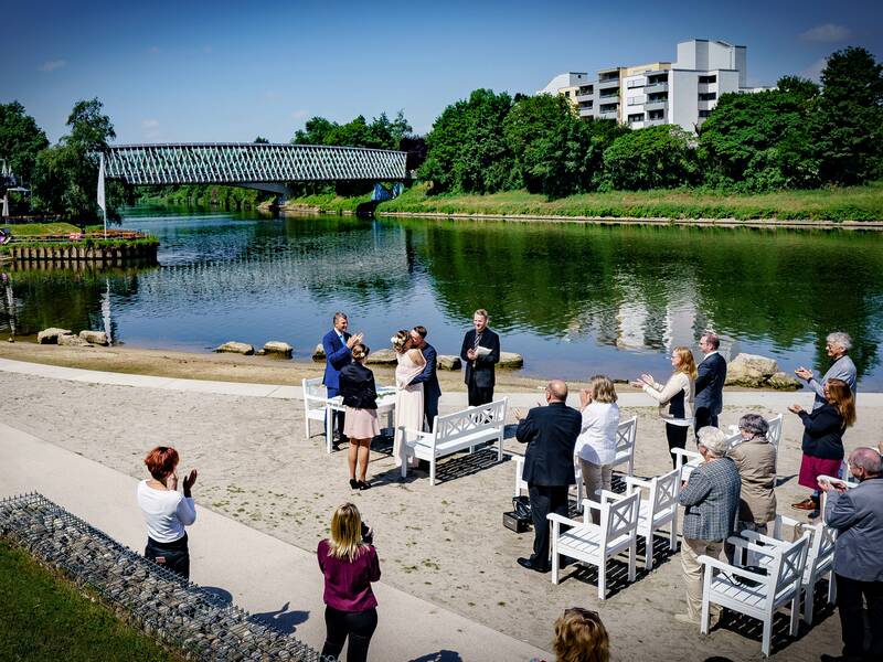 Menschen am NEckarstrand, im Hintergrund fließt der Neckar vorbei und man sieht eine Glasbrücke.