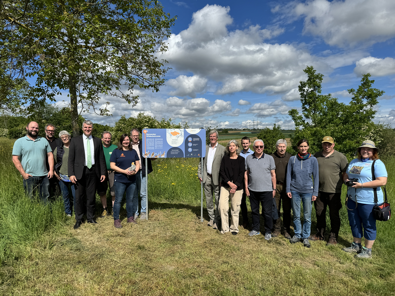 Viele Menschen um eine Infotafel zum Thema Wildschutzzone auf einem Feld.