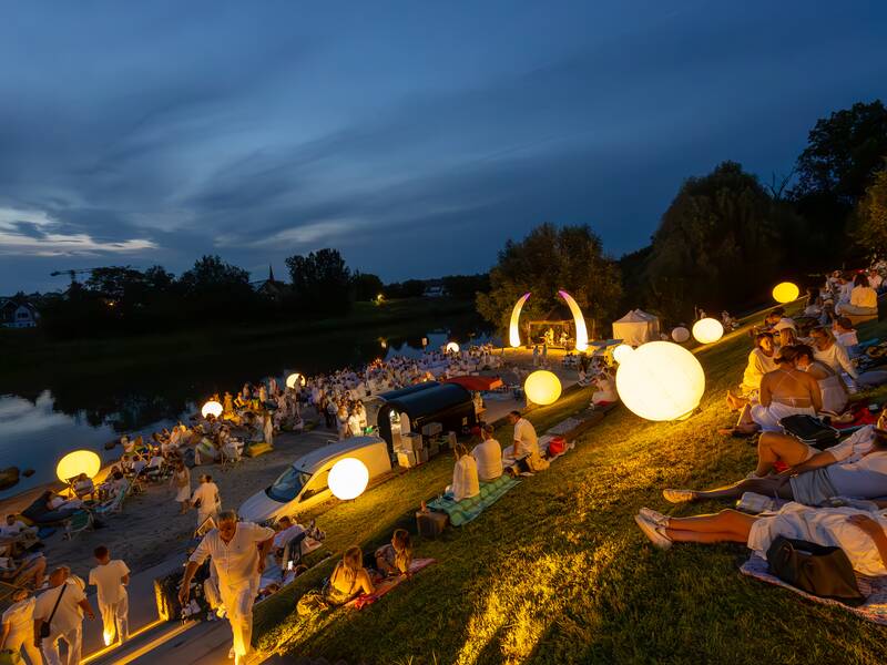 Menschen bei Dämmerung am Neckarstrand. Einzelne Leuchtkugeln geben Licht.