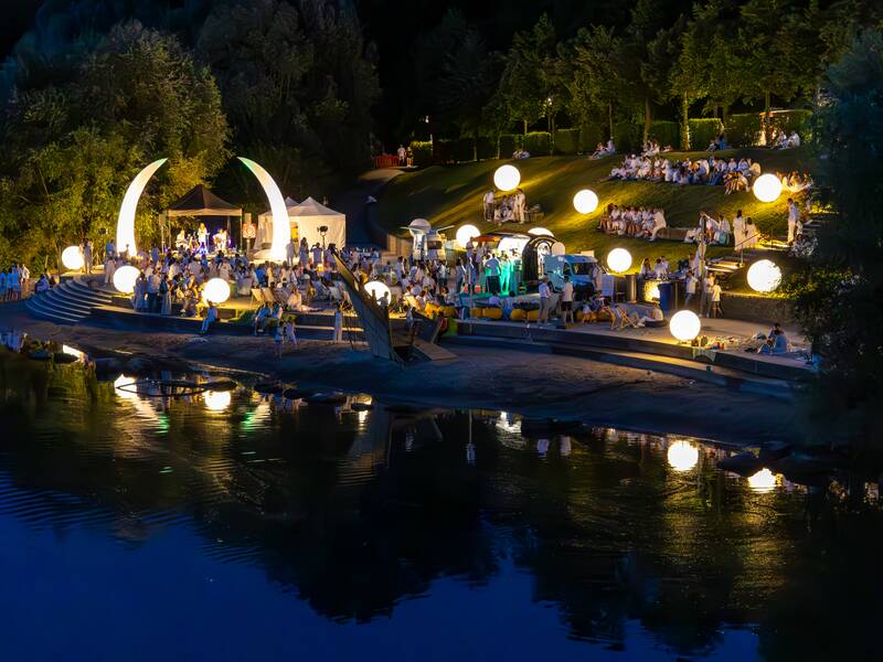 Der Neckarstrand bei Nacht mit einzelnen Leuchtelementen und Personen. Das Licht spiegelt sich im Neckar.