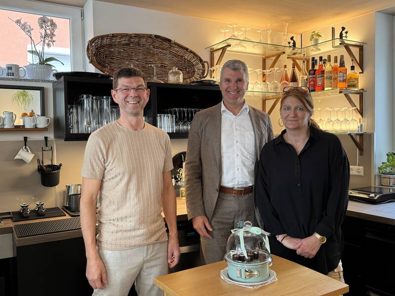 Drei Menschen, darunter OB Dirk Schönberger, stehen in einem Cafe.