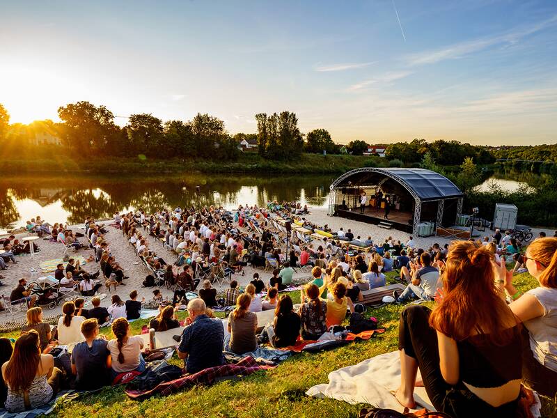 Stadtstrand bei Sonnenuntergang. Strand mit Bühne und vielen Besuchern, die es sich in ungezwungener Atmosphäre gemütlich gemacht haben.