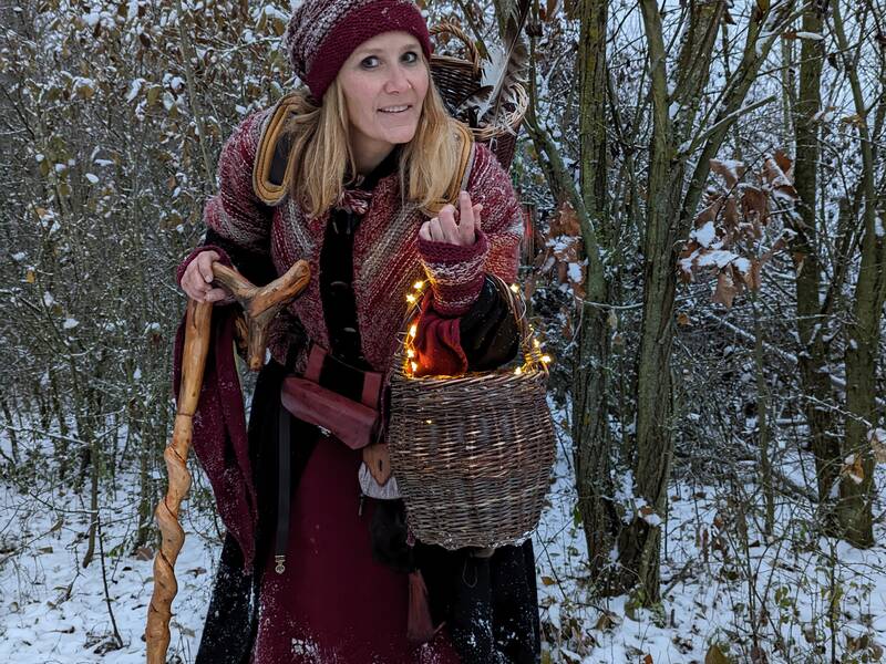 Winterlich gekleidete Frau mit Weidenkorb und Gehstock auf schneebedeckter Wiese