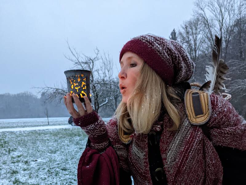 Winterlich gekleidete Frau mit Licht in der Hand auf schneebedeckter Wiese