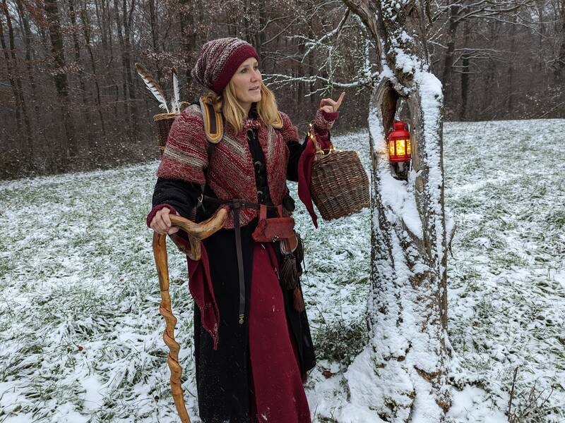 Winterlich gekleidete Frau mit Weidenkorb und Gehstock auf schneebedeckter Wiese